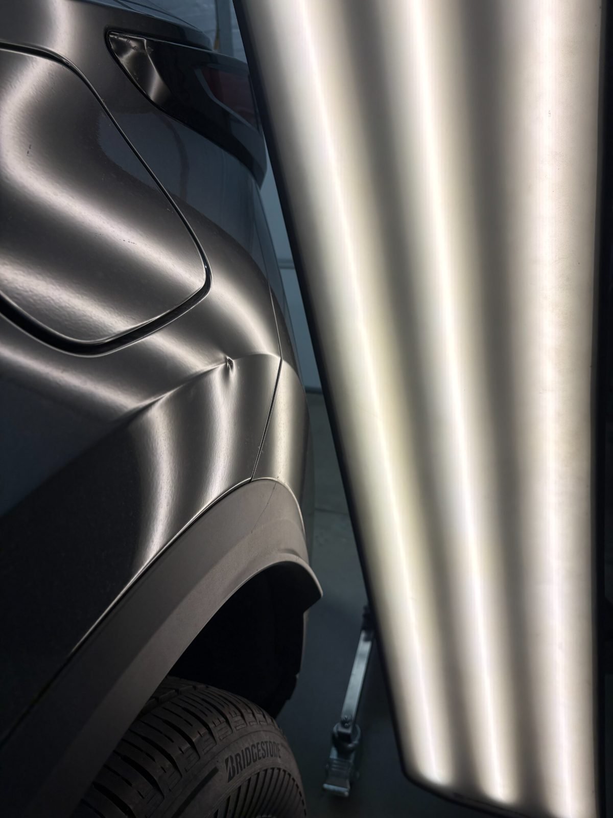 A defined reflected line breaking across hail dents on a painted panel under PDR lighting